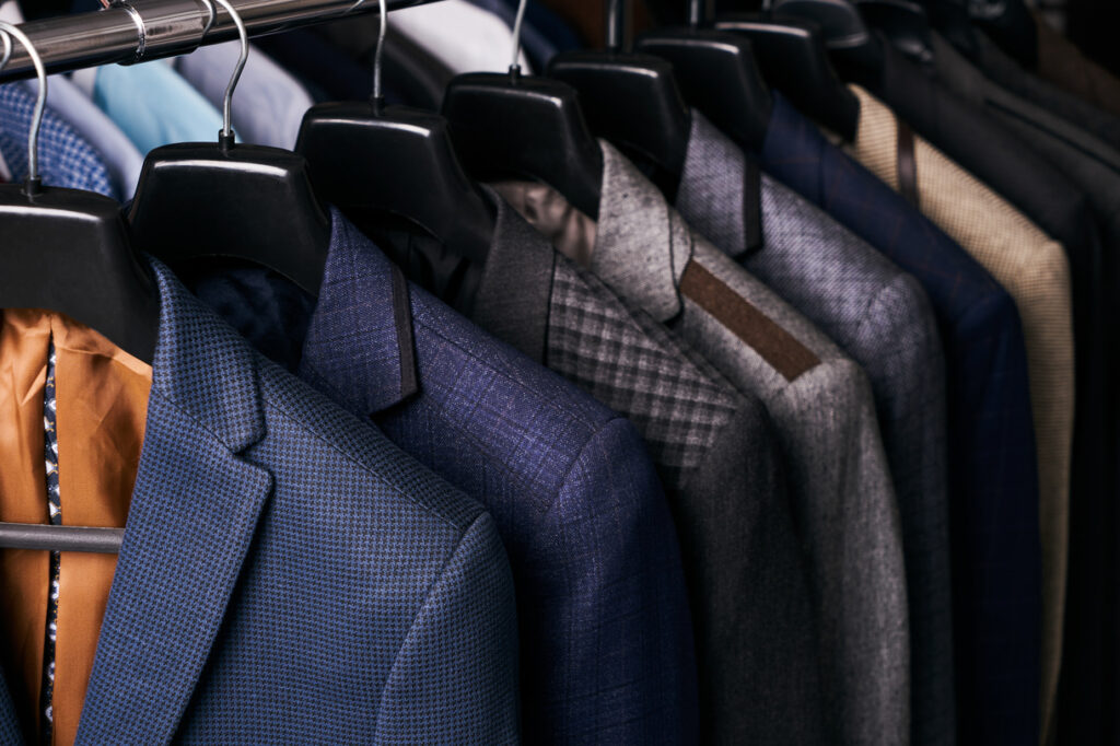 Suits in various colors and patterns hanging on a clothing rack with black hangers.